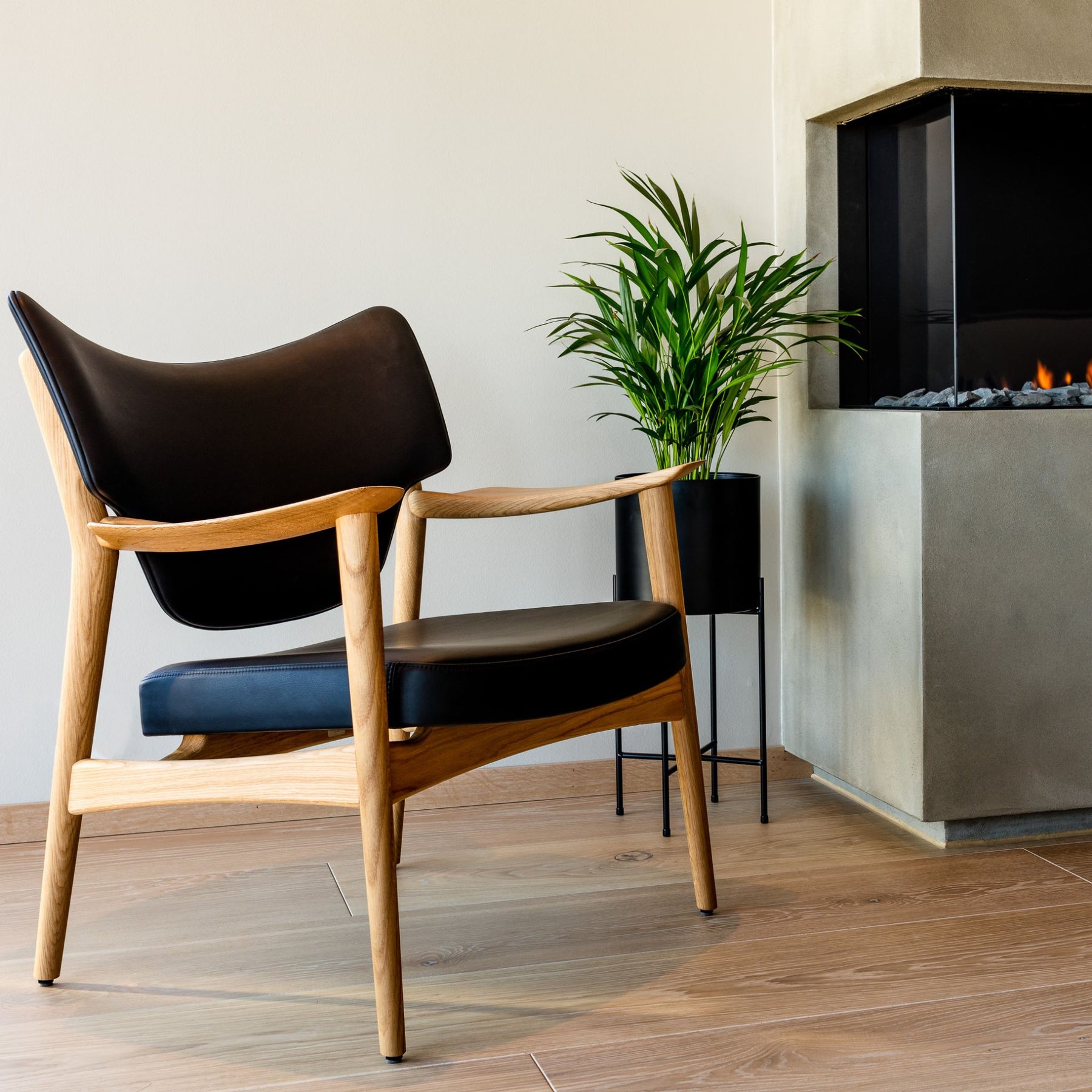 Eikund Veng Lounge Chair Oak with Black Leather in Living Room with Plant by Fireplace